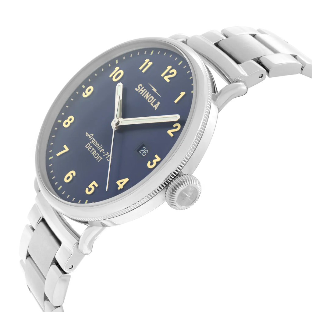An image of a wristwatch viewed from a side profile angle, showcasing its crown prominently. The watch has a stainless steel band and a blue dial with yellow Arabic numerals. The distance is close enough to highlight details, such as the crown's texture and the bracelet links. The watch is labeled as a display model.