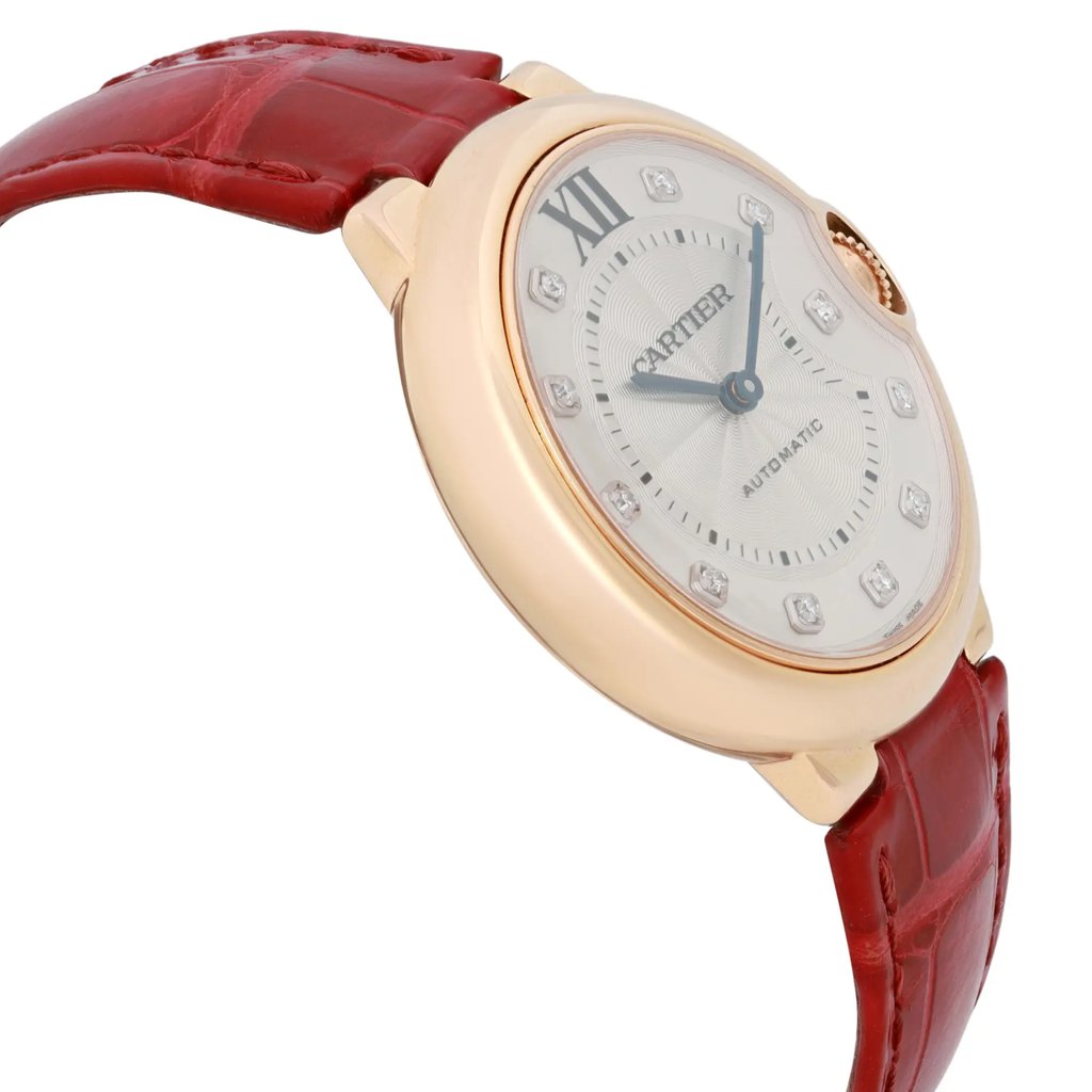An image of a pre-owned Cartier women's wristwatch, captured from a slight angle to the right. The watch features a round, gold-toned case and a silver dial with Roman numeral and diamond hour markers. The red leather strap is partially visible, showcasing its texture. The watch is positioned upright and the image is taken from a close distance, highlighting the intricate details of the watch face and case.