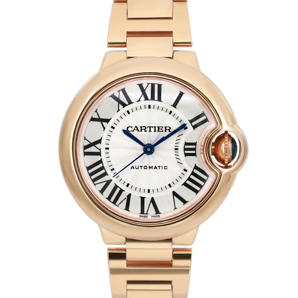 An image of a pre-owned wristwatch taken from a front close-up angle, focusing on the watch face. The watch features a round case with a gold-toned finish and a metallic bracelet. The face is marked with Roman numerals and blue hands, and the brand name is displayed centrally. The crown is uniquely integrated into the case design on the right side.