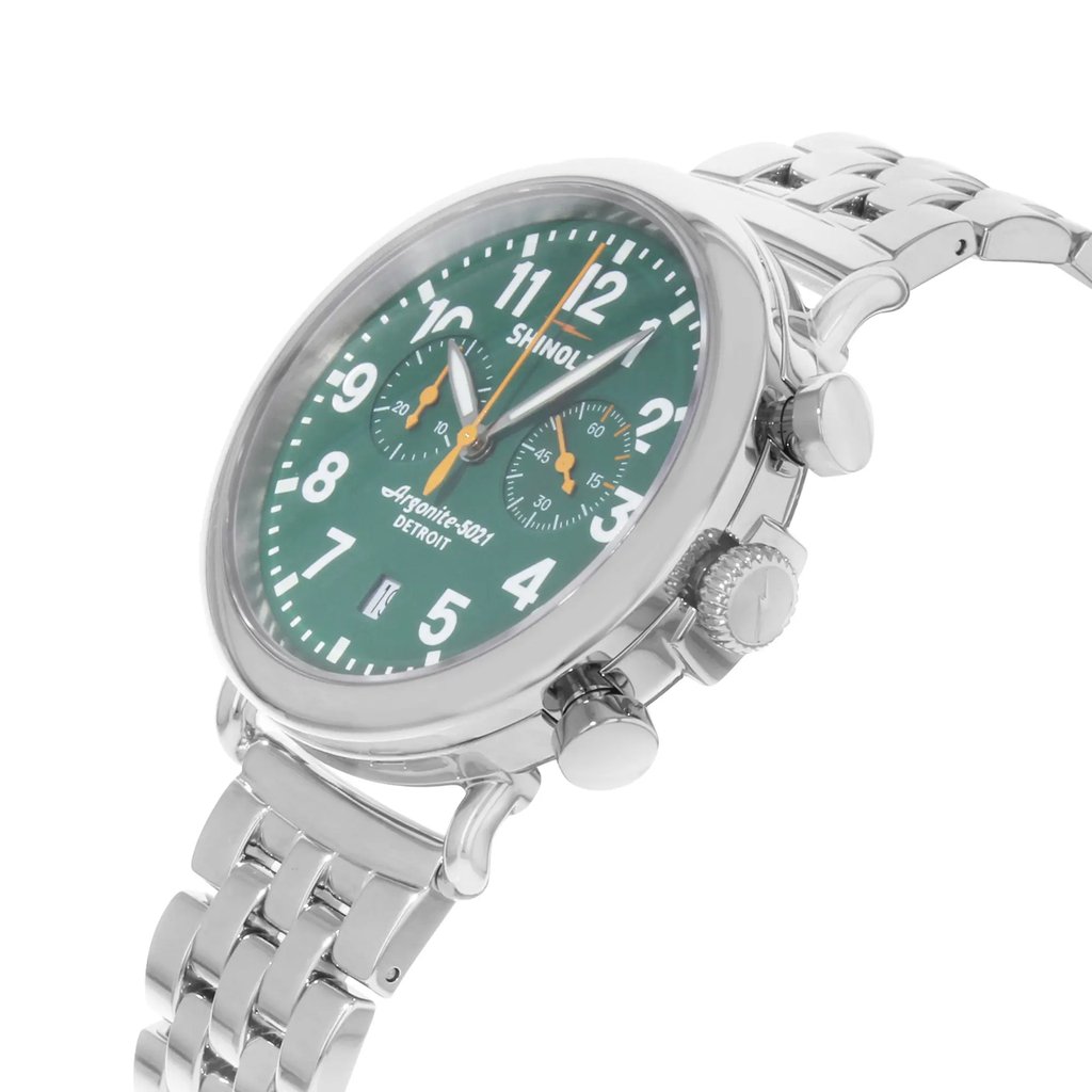 An image of a pre-owned wristwatch shown from a side profile view, highlighting the crown. The watch features a green dial with white numerals and orange accents, and is encased in a polished metal body. The metal bracelet and chronograph buttons are also visible, with the watch positioned at a slight angle, providing a detailed view of its design.