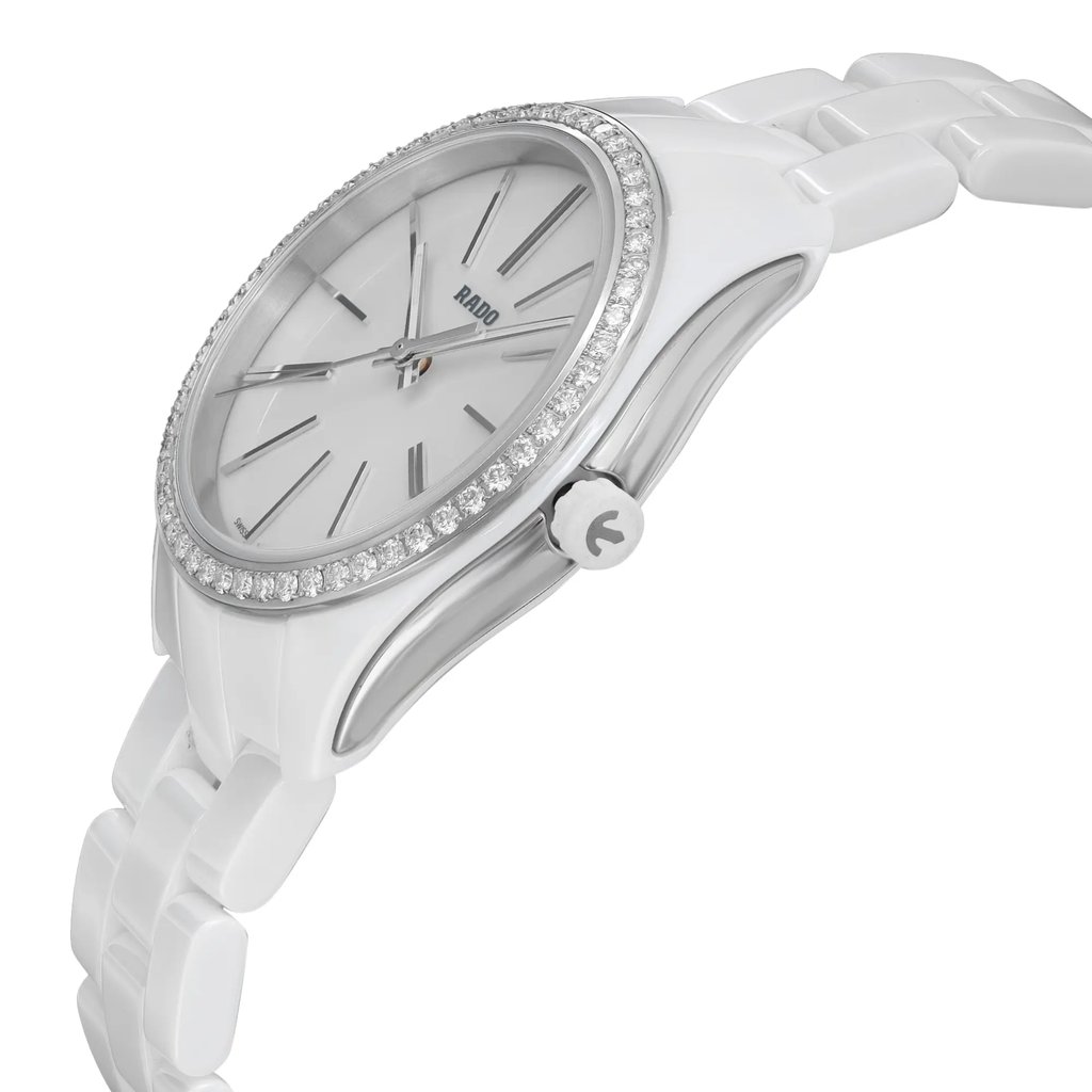 An image of an unworn Rado women's wristwatch in a casual style, captured from a side profile angle that highlights the crown. The watch features a round shape with a white dial and diamond bezel, accented by luminous hands. It is constructed with a ceramic band and case, complemented by stainless steel elements. The watch is positioned at a mid-distance, providing a clear view of the details and craftsmanship.