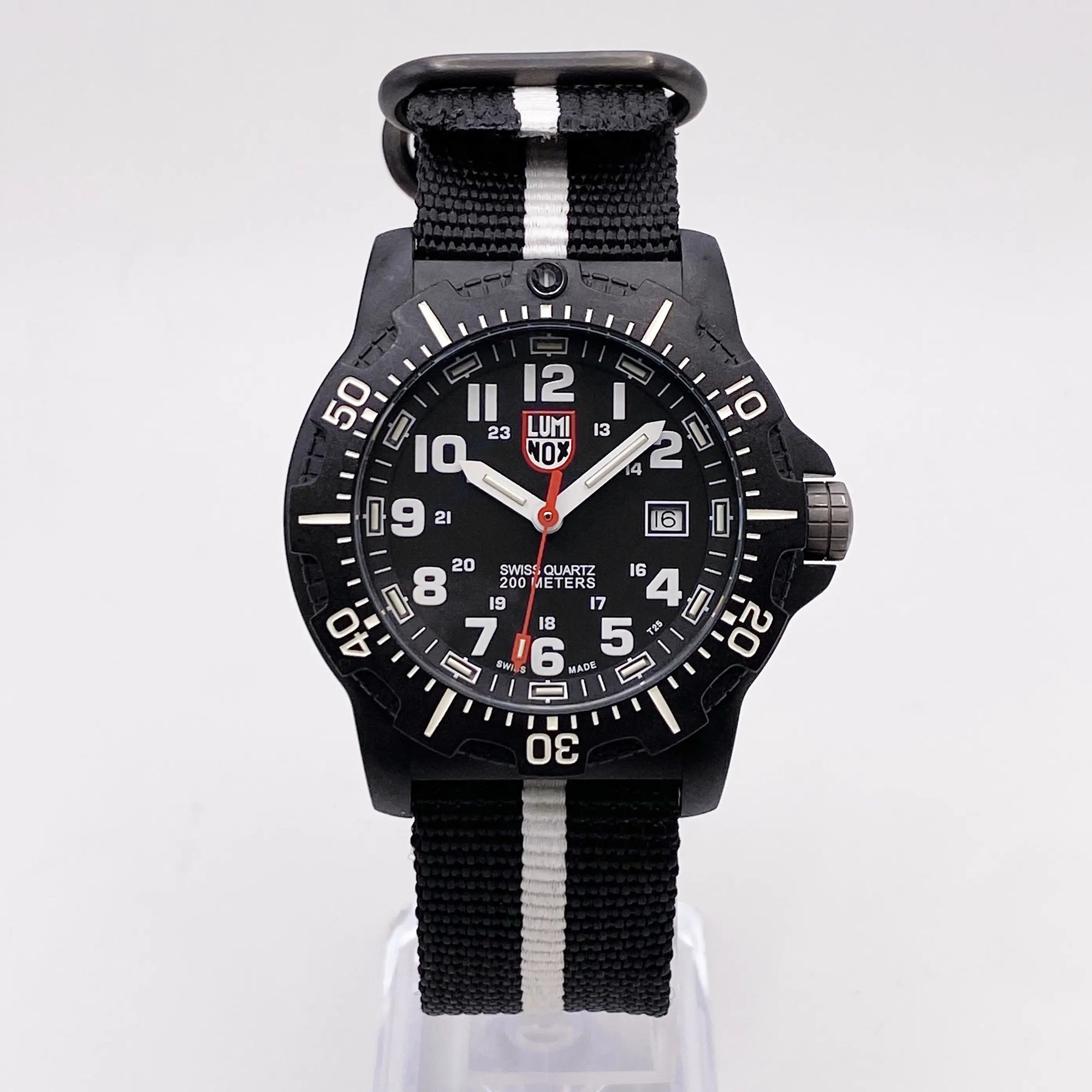 An image of a Wristwatch by Luminox. This Pre Owned item is designed for Men, featuring a Diver,Military style. It has a Quartz movement and an Analog display with a Black dial color. The indices include 12-Hour Dial,Arabic Numerals,Easy to Read/Large Numerals. The band is made of Nylon and the case is made of Carbon. The watch has a Round shape with a case size of 45 mm and a case thickness of 13 mm.