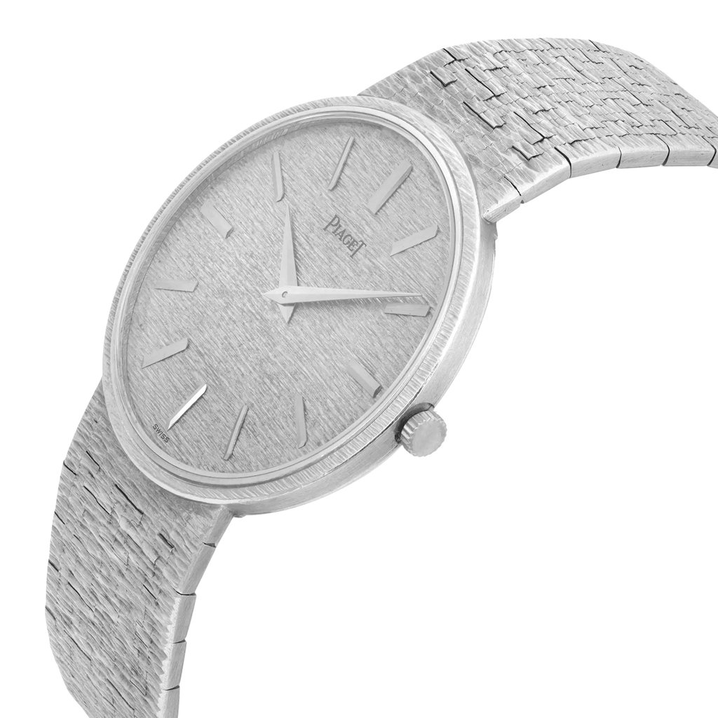 An image of a pre-owned Piaget unisex wristwatch taken from a slightly elevated angle showcasing the watch face and a portion of the bracelet. The watch is positioned at a three-quarter view, highlighting its textured silver dial with minimalist hour markers and hands. The crown is visible on the right side of the case. The image provides a close-up view, emphasizing the intricate details of the watch's design and craftsmanship.