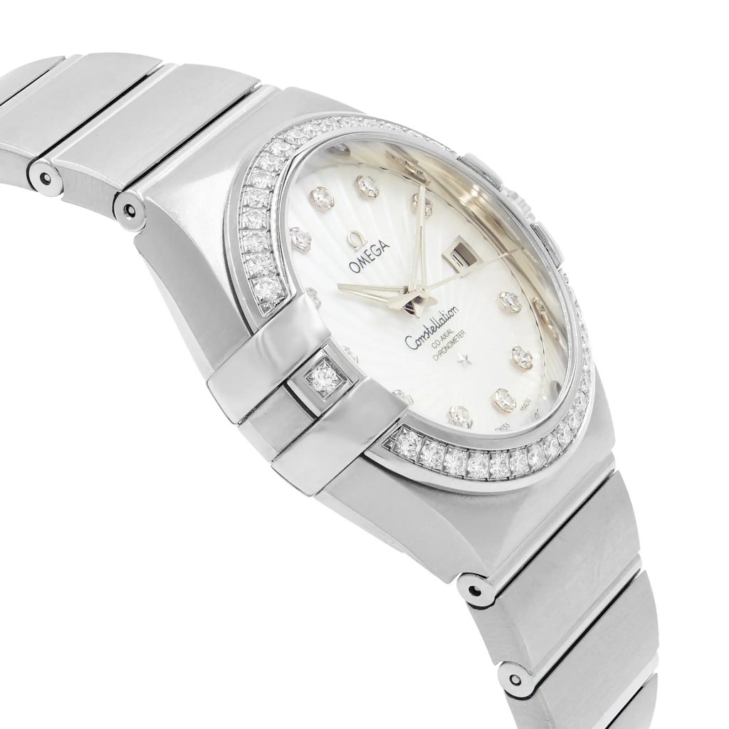 An image of an Omega women's wristwatch captured at a close-up angle, slightly tilted to the right. The watch features a white gold metal bracelet and a round, diamond-studded bezel. The face is elegantly designed with diamond hour markers and a date indicator, showcasing the Omega logo and "Constellation" branding. The watch is presented as a display model, highlighting its refined craftsmanship and luxurious detail.