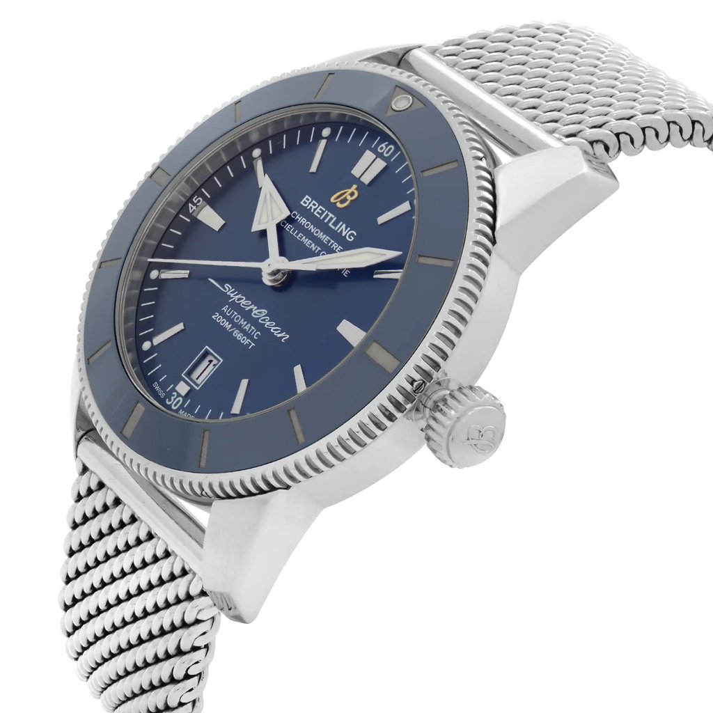 An image of a pre-owned Breitling men's wristwatch with a side profile view emphasizing the crown. The watch features a round stainless steel case and a blue sunburst dial with a matching blue bezel. It is styled as a diver and luxury timepiece with a stainless steel mesh band. The watch is positioned at a slight angle with the crown visible on the right side, and the dial facing slightly upwards, allowing for a clear view of the watch's design and condition. The distance is close-up, providing details of the watch's features. The watch is pre-owned and has light signs of wear and scratches.