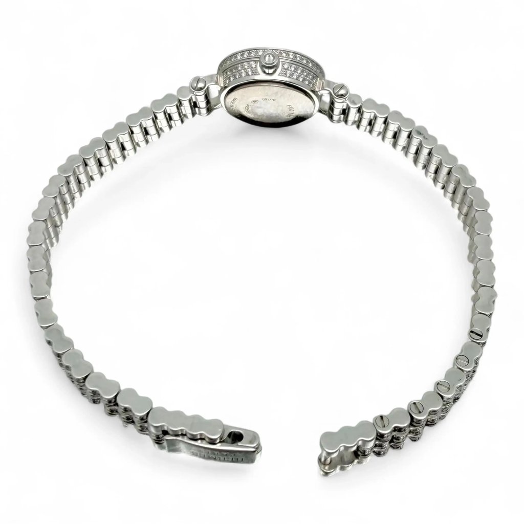 An image of a pre-owned HERMÈS women's wristwatch positioned at a slight angle from the back, displaying the full length of the open metal bracelet. The watch face is tilted downward, showing the side profile of the watch case adorned with small diaminds. The watch is centered against a plain white background, allowing a clear view of its sleek and elegant design from a close distance.