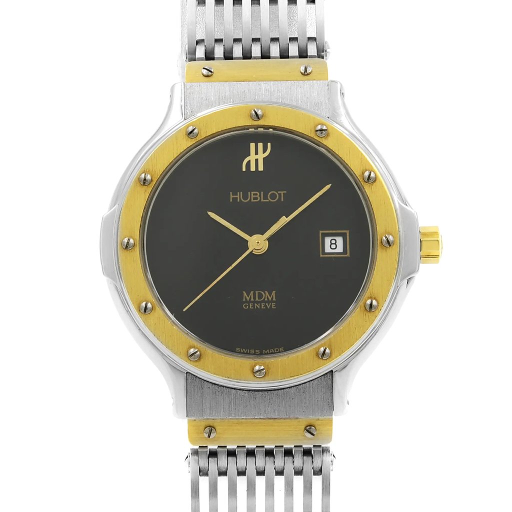 An image of a pre-owned wristwatch taken from a front, close-up angle, showcasing the watch face. The timepiece features a dark dial with gold-toned hands and hour markers. It has a gold and silver bezel, with a date display window at the 3 o'clock position. The watch is attached to a silver metal bracelet, and the brand name "Hublot" is visible on the dial.