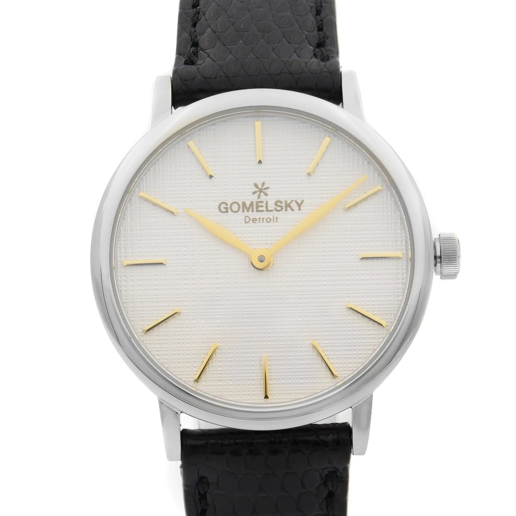 An image of a wristwatch captured from a front close-up angle, showcasing the watch face. The watch features a textured white dial with gold hour markers and hands. The brand name "Gomelsky Detroit" is visible below the 12 o'clock position. The case is silver-toned, and the strap is black with a subtle pattern. The watch is in unworn condition.