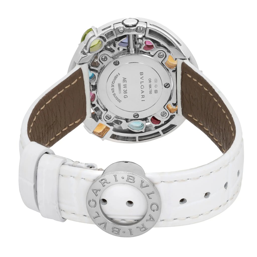 An image of a pre-owned Bvlgari women's wristwatch, positioned upright with a focus on the back of the watch. The angle is slightly elevated, showcasing the intricate details of the watch's back casing, including colorful embellishments around the perimeter. The white leather strap is prominently displayed, with the Bvlgari logo visible on the buckle. The watch is shown from a close distance, highlighting its condition and craftsmanship.