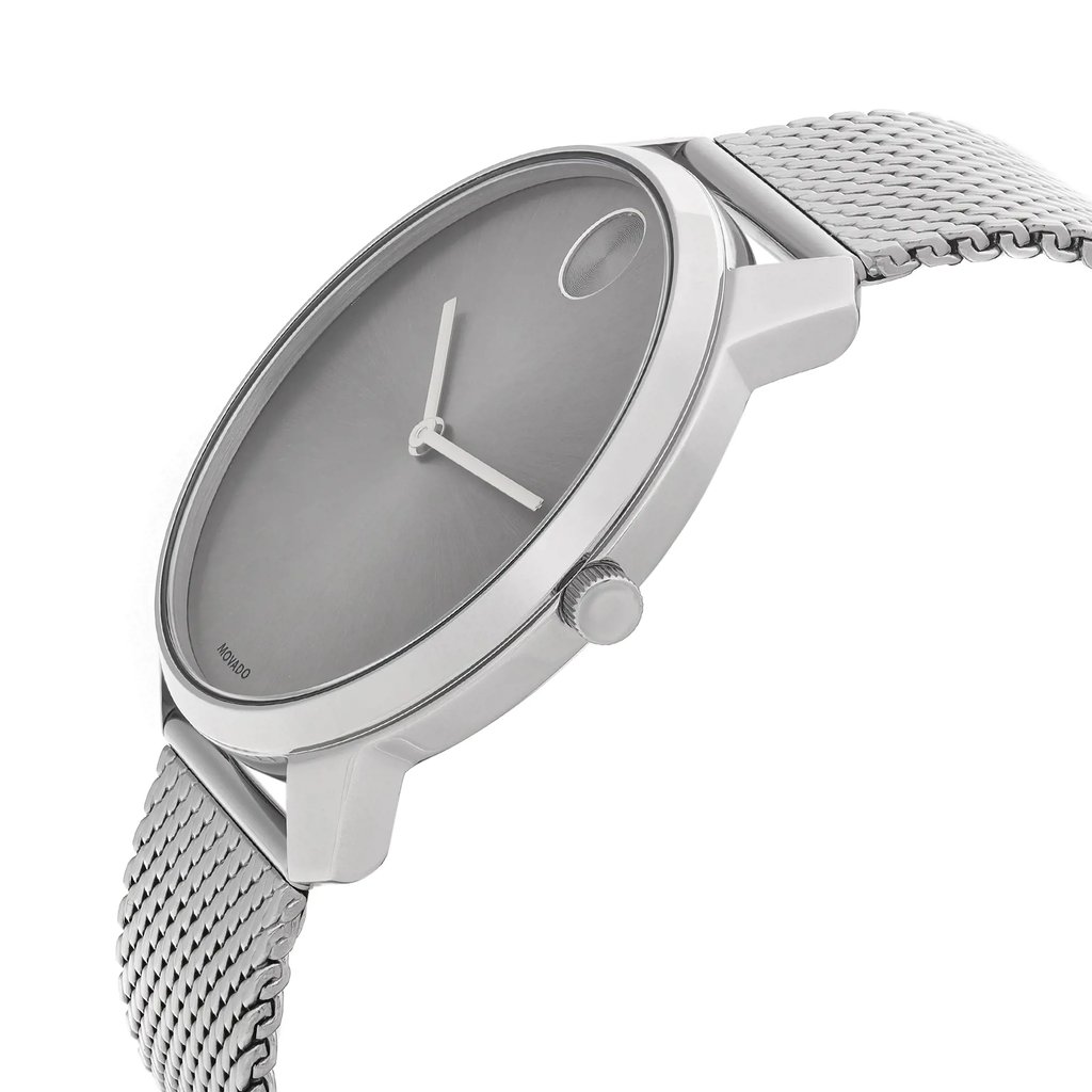 An image of a wristwatch taken from a side profile view, showcasing the watch's crown prominently. The watch has a sleek, minimalistic design with a silver mesh band. The face is simple with two hands and a small dot at the 12 o'clock position. The watch is positioned at a slight angle, allowing a clear view of its elegant structure and details. The image appears to be taken from a moderate distance, focusing on the watch's craftsmanship.