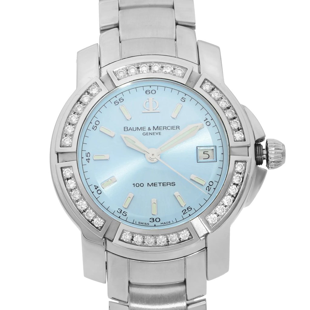 An image of a pre-owned wristwatch taken from a front close-up angle, focusing on the watch face. The watch features a silver metallic bracelet and a light blue dial with silver hour markers and hands. The bezel is adorned with sparkling stones, and the brand name "Baume & Mercier" is visible on the dial. The date window is positioned at 3 o'clock, and the watch is water-resistant up to 100 meters.