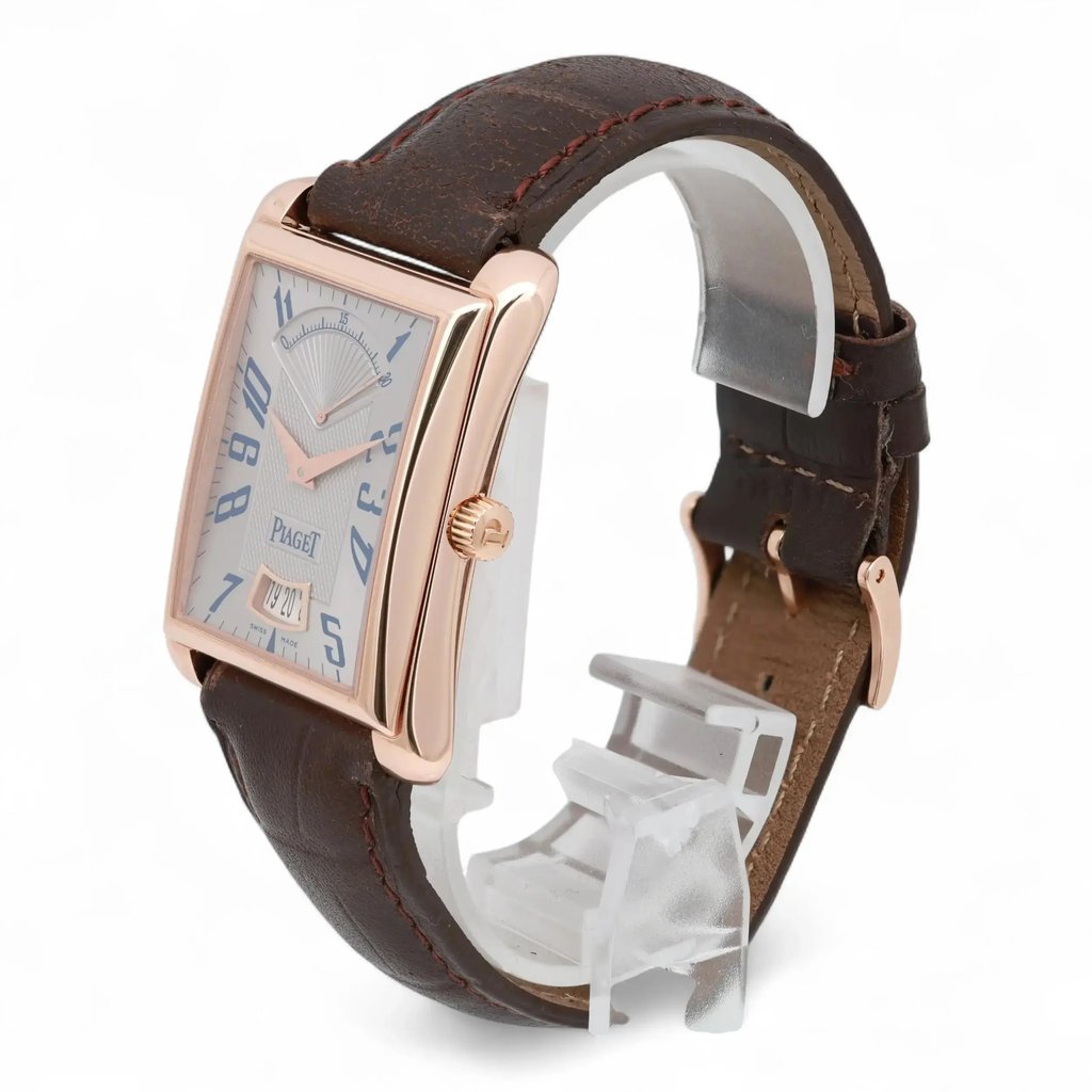 An image of a pre-owned Piaget men's wristwatch positioned at a three-quarter angle, showcasing the front and right side. The watch features a rectangular rose gold case, a brown leather strap, and a clear display with blue numerals and a date window. The image is taken from a moderately close distance, highlighting the elegant design and craftsmanship.