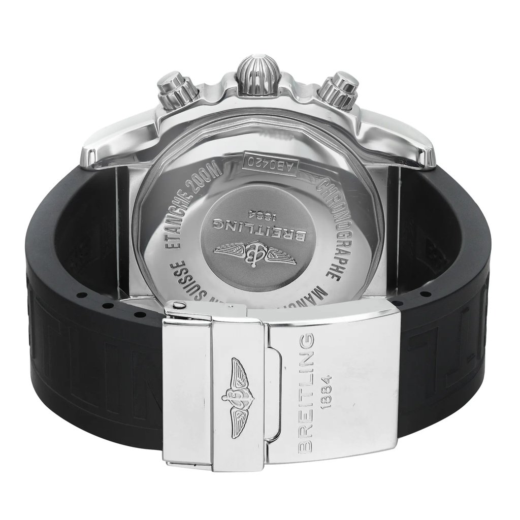 An image of a pre-owned Breitling men's wristwatch, viewed from the back, showcasing the solid stainless steel caseback and rubber band. The watch is positioned with the caseback facing up and the deployant clasp of the band open and angled to the right side, providing a clear view of the Breitling logo on the clasp. The distance is close enough to reveal the text and engravings on the caseback and clasp in detail. The band may show minor signs of wear.