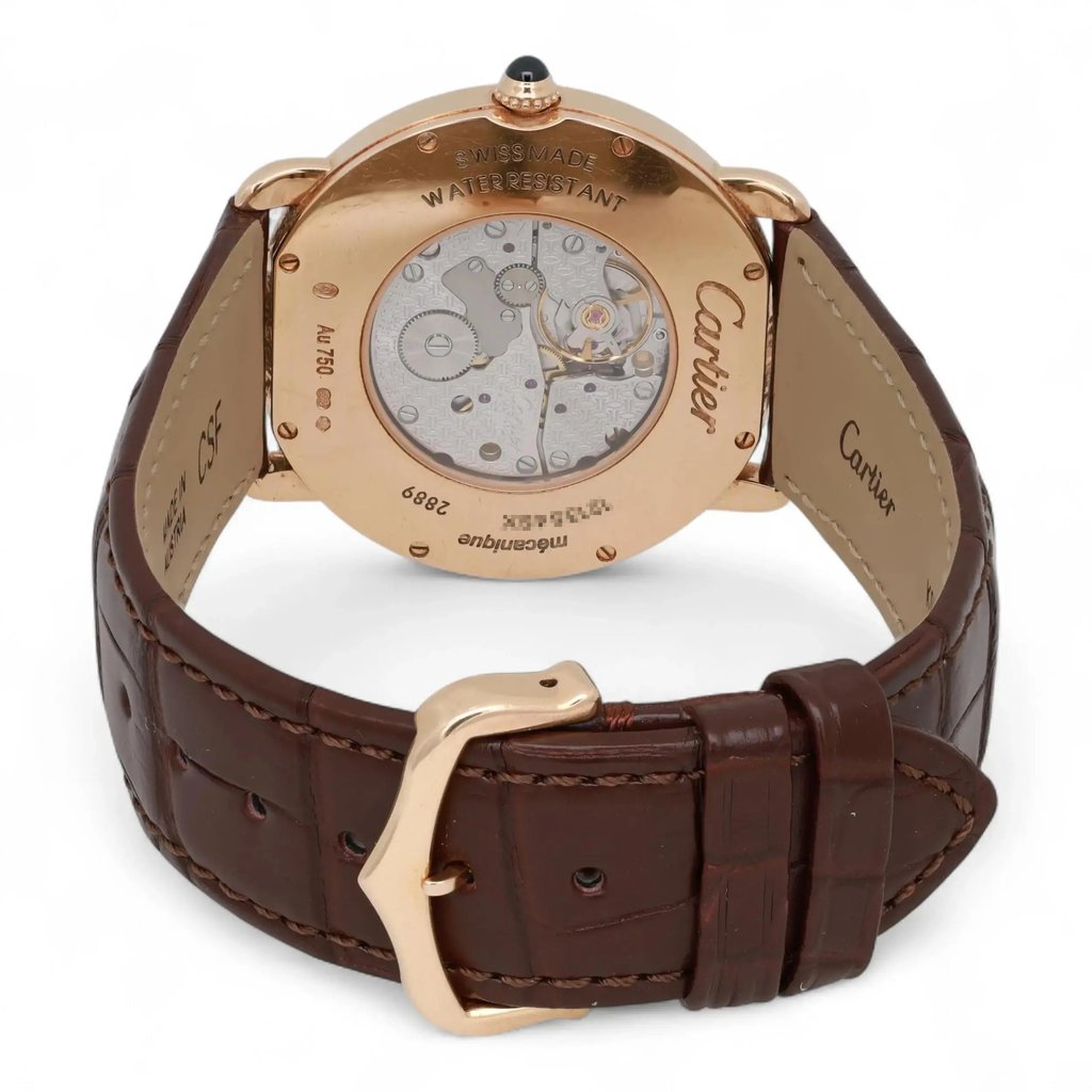 An image of a pre-owned Cartier unisex adult wristwatch. The watch is positioned at a slight angle, showcasing the back view. The case is rose gold with visible engravings, and a clear display reveals the intricate internal mechanisms. The watch is fitted with a dark brown leather strap, and the gold buckle is prominently displayed in the foreground. The photograph is taken from a close distance, highlighting the details of the watch's craftsmanship.