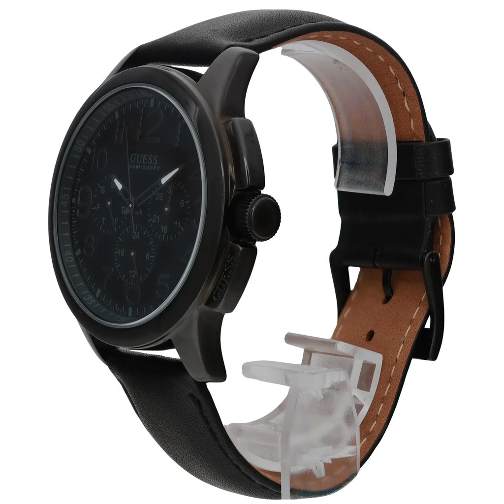 An image of a pre-owned men's GUESS wristwatch, featuring a chronograph, date indicator, day/date function, luminous hands, and a small seconds subdial. The watch is positioned at a slight angle, displaying the face and side profile, with the strap partially curved and visible. The watch is photographed from a medium distance, highlighting its black leather strap and dark watch face.