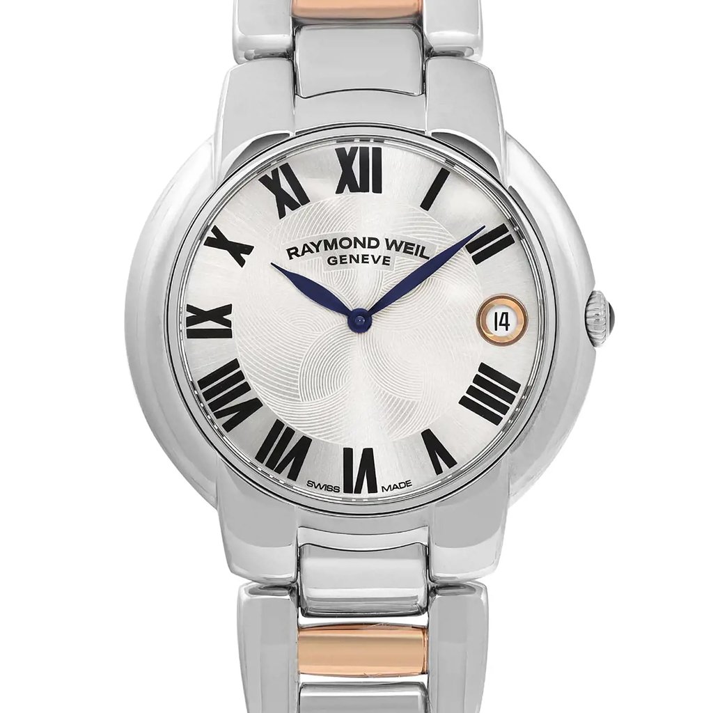 An image of a pre-owned RAYMOND WEIL women's wristwatch in good condition, presented in a close-up front view that highlights the watch face. The watch features a round stainless steel case and a matching stainless steel band, with a dress/formal style. The dial is silver with a floral pattern and is adorned with black Roman numerals as indices. It has blue hands and includes a date indicator at the 3 o'clock position. The bezel is also made of steel, complementing the overall design. The image is taken from a front angle, showing the watch face and a portion of the band, with the timepiece centered and occupying the majority of the frame.Pre-owned and in good condition. The watch only has tiny scratches on the rose-gold links.

