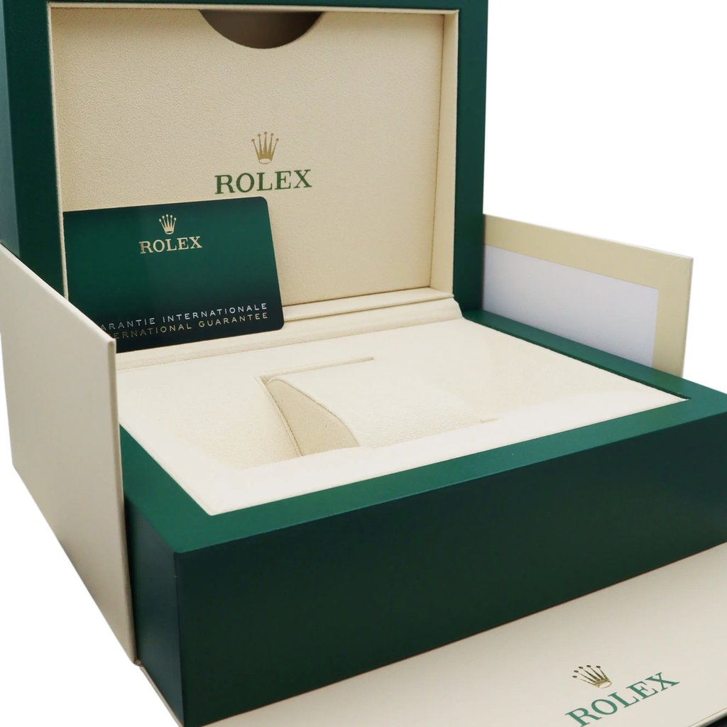 An image of an unworn wristwatch packaging, viewed from a slightly right-angled perspective at a close distance. The box is open, revealing a beige interior with a green outer edge. A green international guarantee card is positioned inside the box, which prominently features the Rolex logo in gold.