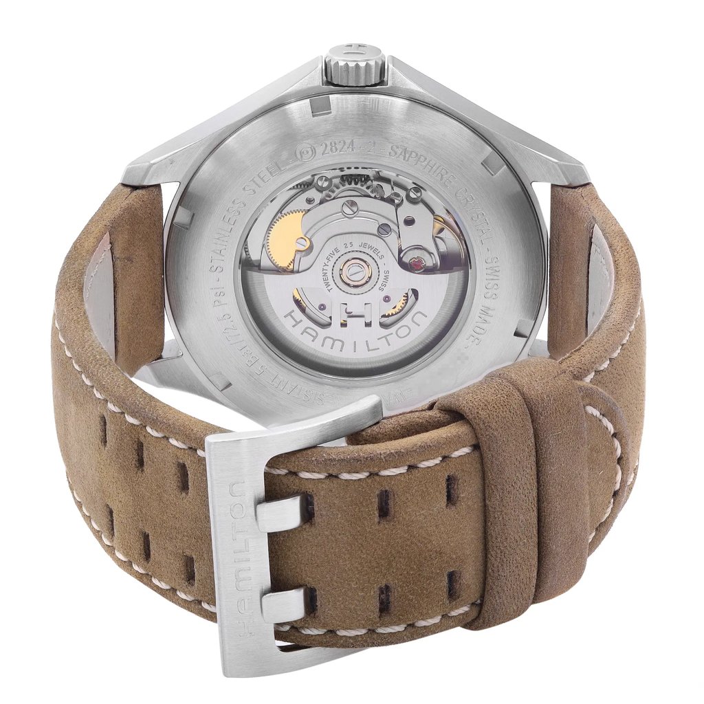 An image of a wristwatch viewed from the back, showcasing the intricate mechanical movement through a transparent case back with "Hamilton" branding. The watch is positioned upright, with the tan leather strap and clasp visible at a close angle. The stitching on the strap is detailed, highlighting its display model condition.