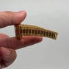 An image of a pre-owned women's Rolex wristwatch held between two fingers. The focus is on the gold bracelet, viewed from the side at a close distance, showcasing its metallic links and its stretch.