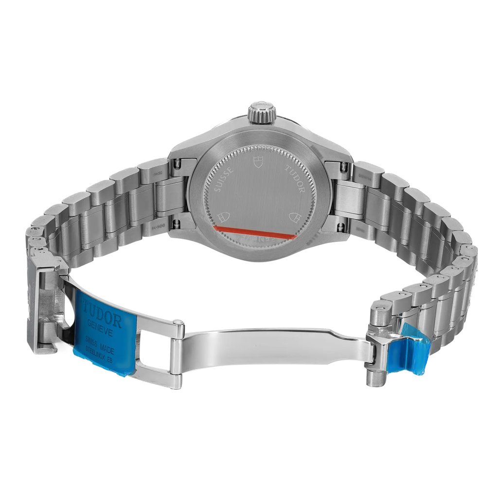 An image of a wristwatch showing a back view with an open clasp. The watch is positioned centrally with the camera capturing it from a slightly elevated angle. The distance allows for a clear view of the unworn stainless steel bracelet and the watch's back case. The clasp is open, revealing the brand's markings and protective blue stickers on the links.