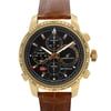 An image of a pre-owned Chopard men's wristwatch, positioned upright with a front-facing angle. The watch features a yellow gold case and a brown leather strap. The black dial includes a chronograph, date indicator, luminous hands, and a small seconds subdial, all visible at close range.