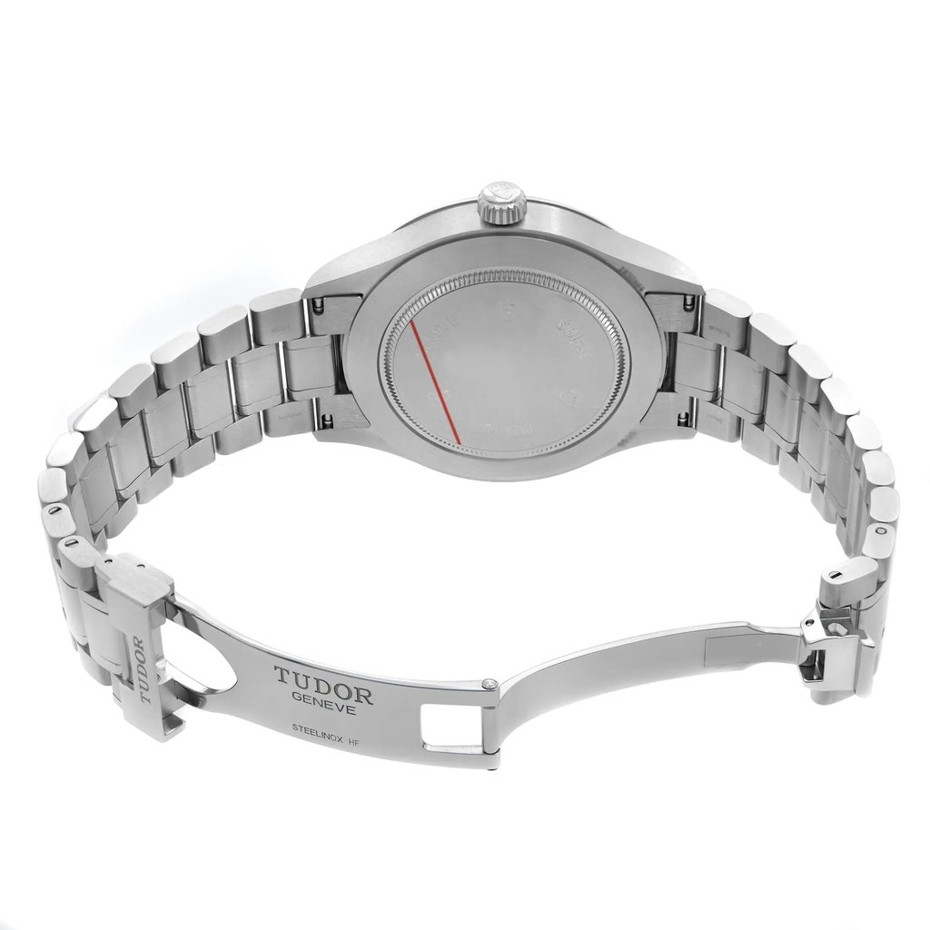 An image of a pre-owned Tudor men's wristwatch viewed from the back, showcasing the stainless steel bracelet and clasp. The watch is positioned at a slight angle, offering a clear view of the closed case back and the Tudor branding on the clasp. The photo is taken from a moderate distance, highlighting the craftsmanship and details of the bracelet links and the engraved text on the clasp.
