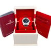 An image of an unworn women's OMEGA wristwatch displayed in an open box. The watch, featuring a date indicator and luminous hands, is positioned upright on a red cushion inside a white box with a textured exterior. To the left, a red booklet labeled "OMEGA Operating Instructions" is visible. On the right, there are red documents with visible text. The angle is straight-on, capturing the full view of the box and its contents at a close distance.