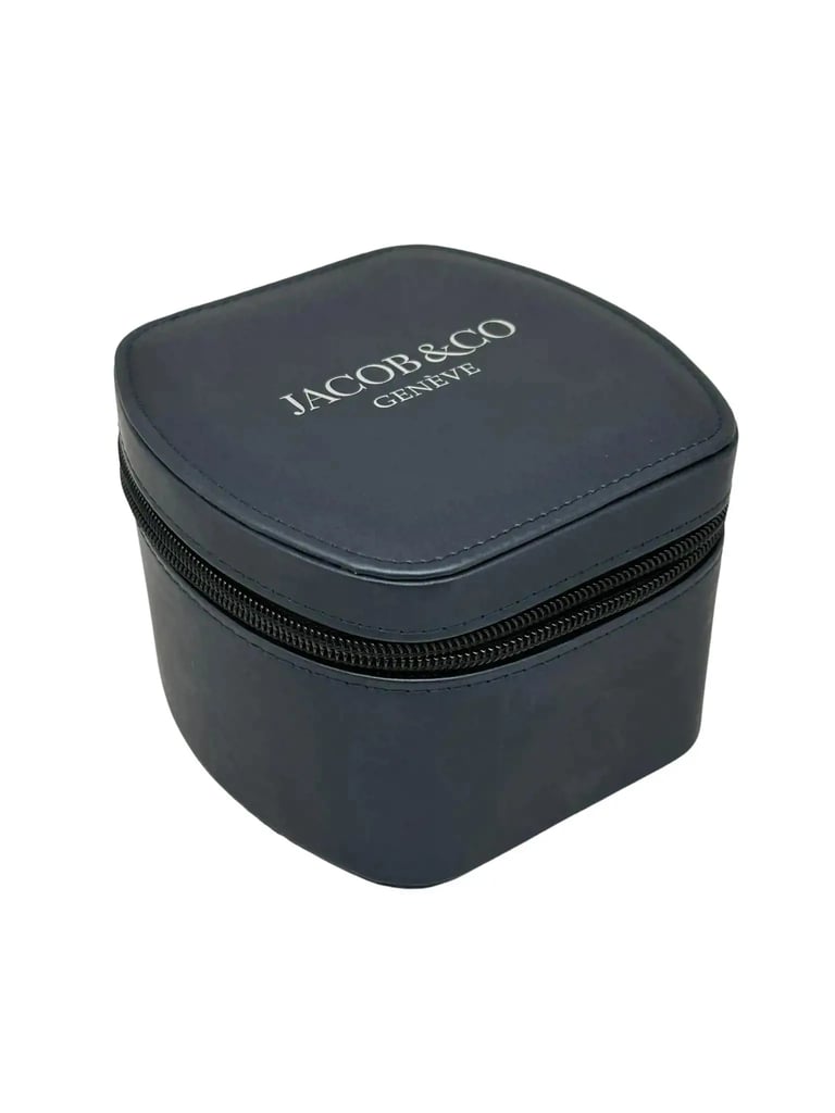 An image of a wristwatch box positioned at a slight angle, displaying a three-quarter view from a close distance. The box is dark in color with the brand name "Jacob & Co Genève" printed on the top. It features a zippered closure and has a smooth, rounded design. The photograph focuses solely on the box, with no watch visible.