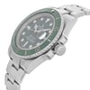 An image of a pre-owned wristwatch taken from a side profile view, highlighting the crown prominently. The watch has a metallic bracelet and a green bezel. The angle captures the thickness of the case and the detailed design of the crown, with the watch face partially visible. The photograph is taken from a relatively close distance, showcasing the watch's features clearly.