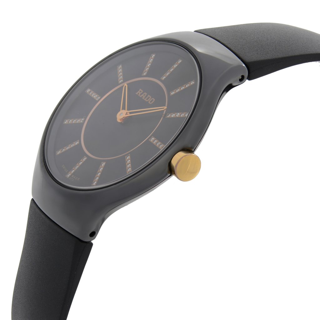 An image of a wristwatch shown from a side profile view, highlighting the crown prominently. The watch face is angled slightly, revealing a sleek design with a dark dial and gold accents. The wristband is visible and appears to be made of a smooth material. The photograph is taken at a close distance, emphasizing the watch's new condition despite having defects.