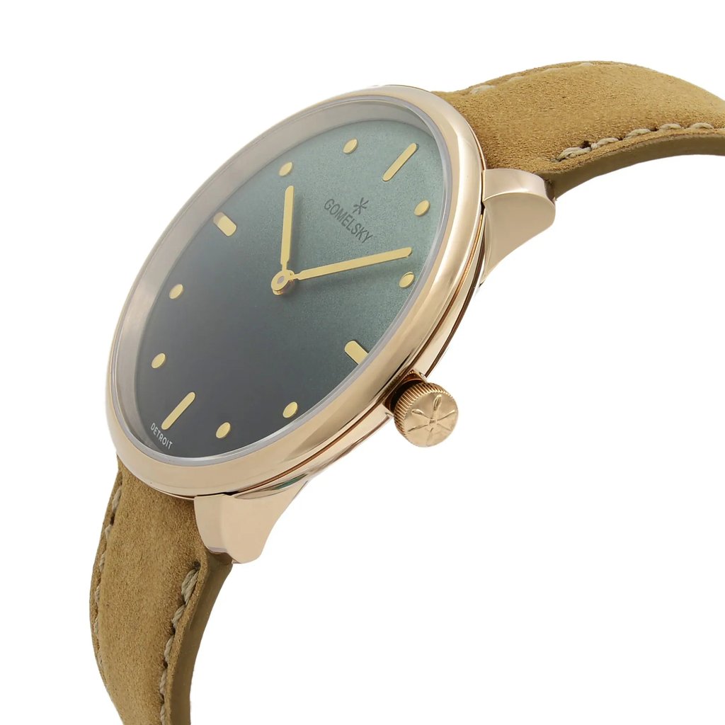 An image of a wristwatch in an unworn condition, viewed from a side profile angle. The focus is on the crown, which is prominently displayed. The watch features a sleek design with a gold-tone case and a smooth, olive green dial. The strap is a light brown suede, adding a touch of elegance. The image captures the watch from a close distance, highlighting its detailed craftsmanship.