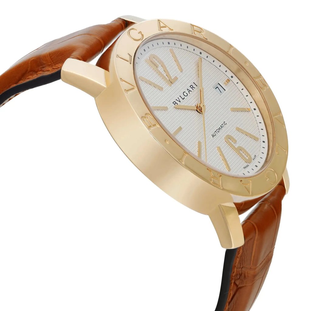 An image of a pre-owned Bvlgari men's wristwatch taken from a slightly angled side view, showcasing the watch's gold-toned bezel and white dial. The dial features gold hour markers and hands, with a date indicator at the 3 o'clock position. The brown leather strap is visible, adding a classic touch to the design. The photo is taken at a close range, emphasizing the watch's elegant details and craftsmanship.