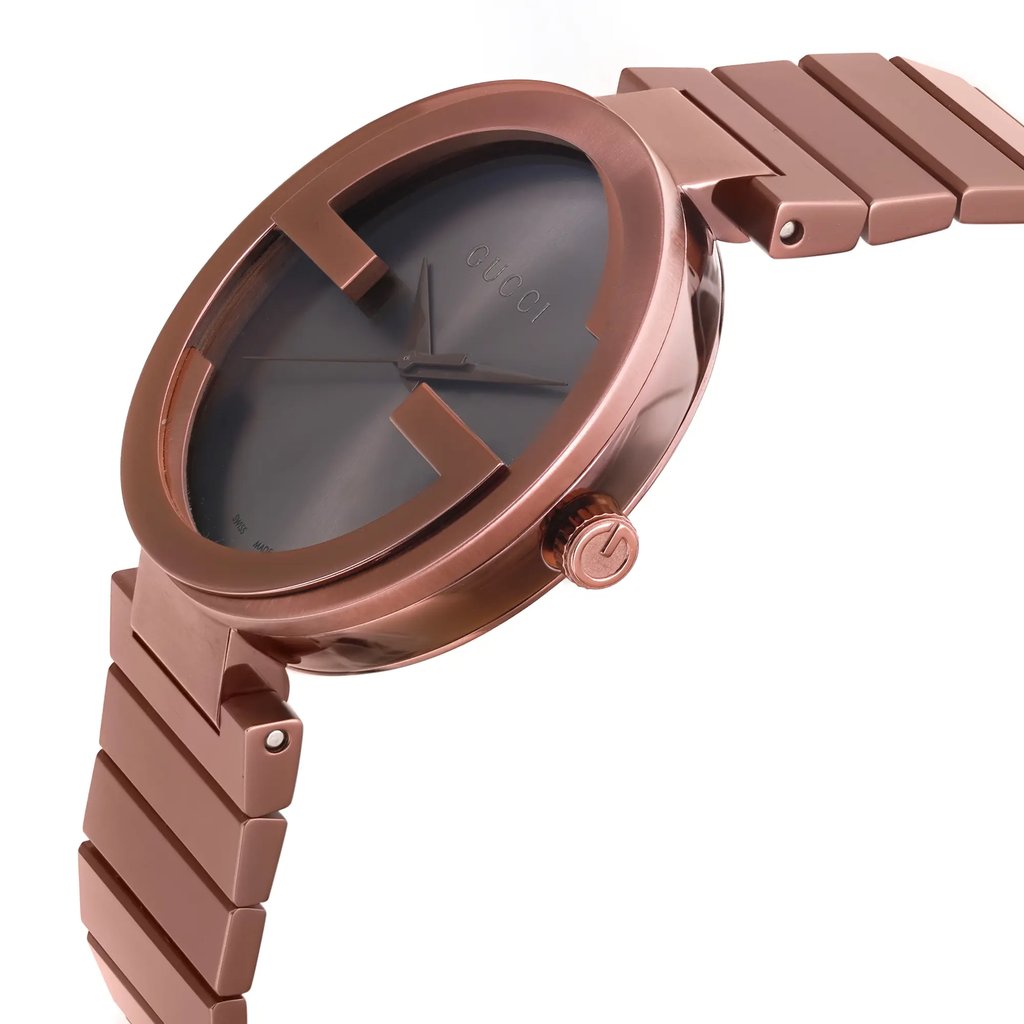 An image of a men's Gucci wristwatch in display model condition, shown in a side profile view with the crown visible. The watch has a casual style with a brown dial and bezel, and is constructed from stainless steel. The band is also made of stainless steel, and the round case of the watch is captured at a close distance, emphasizing the metallic brown finish and the brand name on the dial.