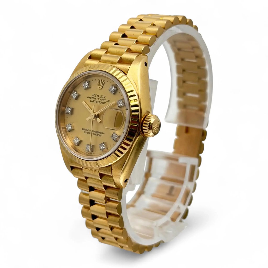 An image of a pre-owned women's Rolex wristwatch, positioned at a slight angle to the left, showcasing its elegant gold finish. The watch is captured at a medium distance, highlighting its date indicator feature and diamond hour markers on the dial. The bracelet is prominently displayed, emphasizing the watch's luxurious design.