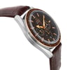 An image of a pre-owned wristwatch shown from a side profile view, opposite the crown. The watch features a brown leather strap and a metallic case. The face of the watch is angled slightly upward, displaying a dark dial with multiple sub-dials and orange accents. The tachymeter scale is visible around the bezel. The image is taken at a close distance, highlighting the watch's details and craftsmanship.