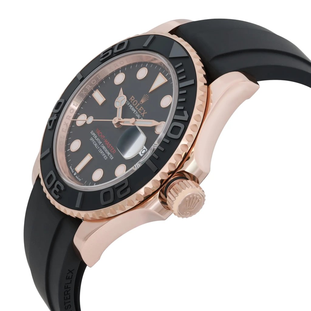 An image of a pre-owned men's Rolex wristwatch, viewed at a slight angle from the front and side. The watch features a black dial with a date indicator and luminous hands. Its rose gold case contrasts with a black bezel and strap. The focus is on the crown and the side of the watch, highlighting its detailed craftsmanship.