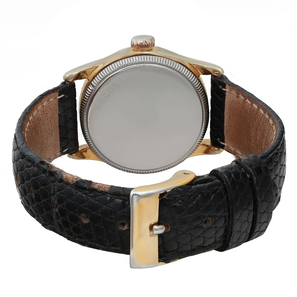 An image of a pre-owned women's Rolex wristwatch viewed from the back at a slightly elevated angle. The watch features a gold-tone case and a black textured leather strap with a gold buckle. The watch face is not visible, and the focus is on the clasp and strap. The background is plain, emphasizing the watch's details.