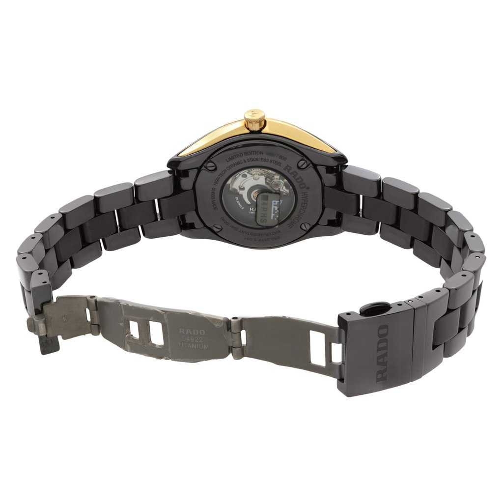 An image of a pre-owned women's Rado wristwatch, viewed from the back with an open clasp. The watch features a round shape with a case made of ceramic and stainless steel. The exhibition caseback reveals the inner workings, while the band is crafted from ceramic. The fold-over clasp with a double push button is open, showcasing the closure mechanism. The watch includes a date indicator and luminous hands. The angle captures the watch from a slight distance, emphasizing the details of the band and clasp.