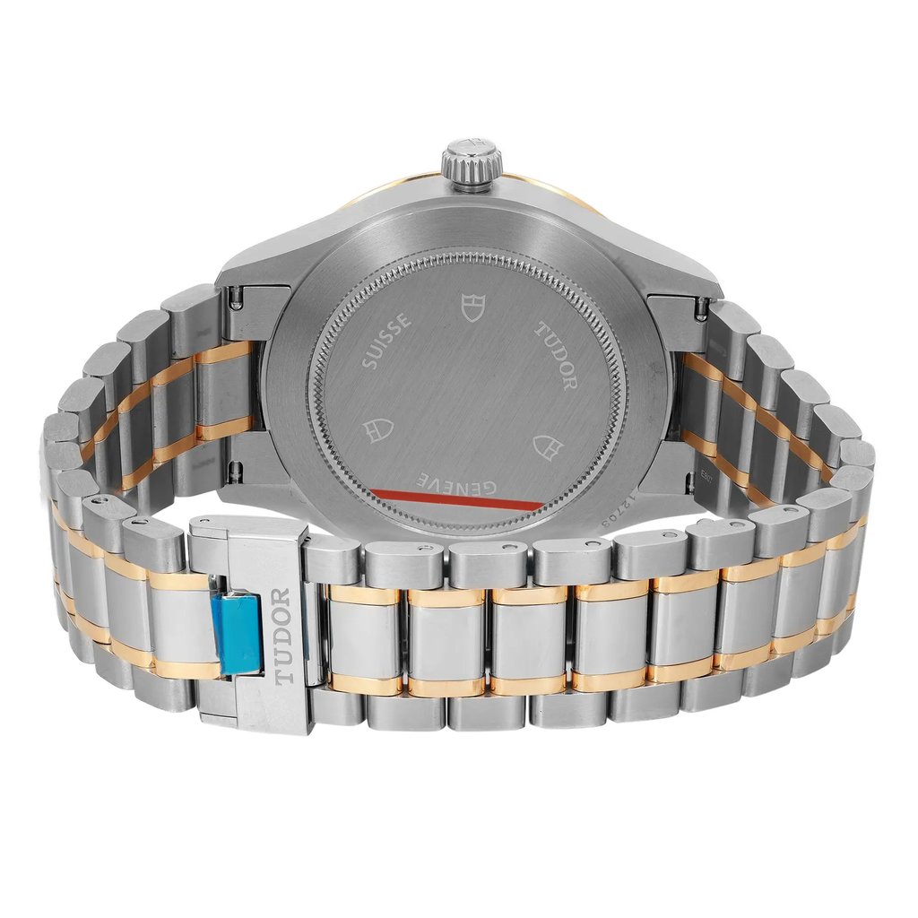 An image of a wristwatch showing the back view with a focus on the closed clasp. The watch features a two-tone metal bracelet with silver and gold links. The back case is visible, displaying engraved details, and the condition appears unworn. The clasp prominently displays the brand name. The angle is slightly elevated, capturing the watch at a close distance.