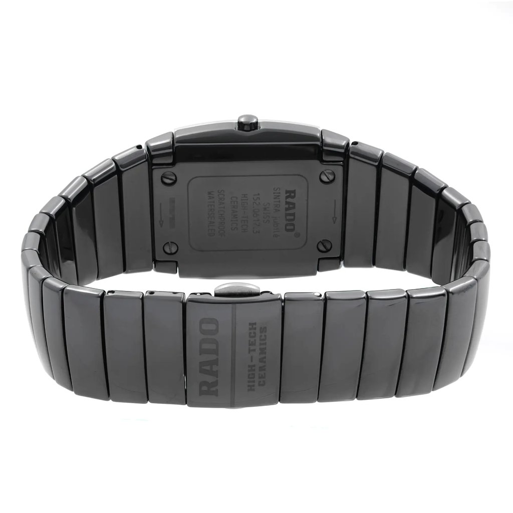 An image of a pre-owned wristwatch showing the back view with a closed clasp. The watch is positioned centrally, captured from a straight-on angle at a close distance. The shiny ceramic bracelet and engraved details on the clasp and case back are clearly visible.