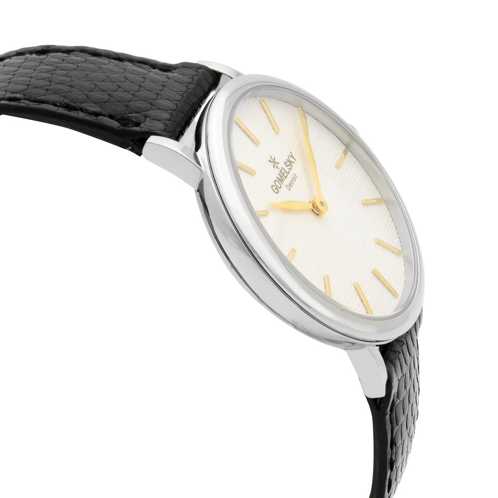 An image of a wristwatch shown from a side profile view, opposite the crown. The watch is unworn and features a sleek, polished metal case. The dial is light-colored with gold hour markers and hands, set against the textured background. The watch strap is black with a textured pattern, adding a sophisticated touch. The angle highlights the thinness of the watch case and provides a close-up perspective on the elegant details.