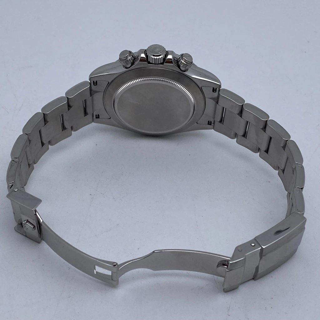 An image of a pre-owned men's Rolex wristwatch positioned at an angle, showcasing the back of the watch. The focus is on the clasp and bracelet, which are partially open, allowing a view of the watch's rear casing. The chronograph buttons and crown are visible on the side, with the image taken at a close distance, highlighting the metallic sheen and design details.