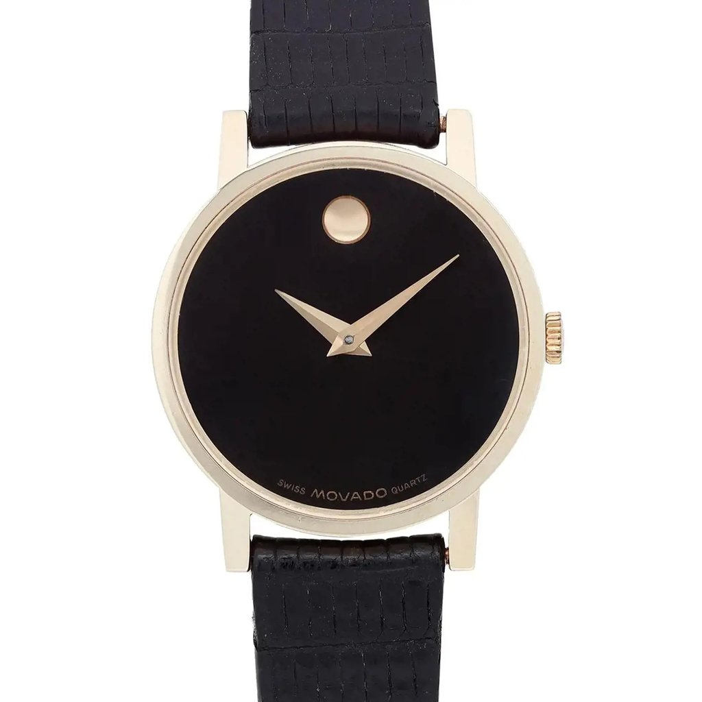 An image of a pre-owned wristwatch taken from a front close-up angle, focusing on the watch face. The watch features a black dial with minimalist design elements, including a single gold dot at the 12 o'clock position and gold hands. The case is gold-toned, and the watch is attached to a textured black strap.