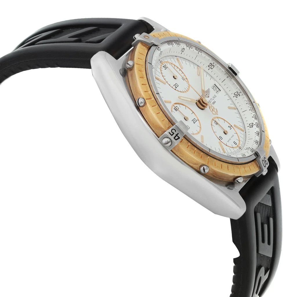 An image of a pre-owned Breitling men's wristwatch in a casual style, shown in a side profile view from the opposite side of the crown. The watch features a round stainless steel case with a gold-colored bezel that has minor nicks, a white dial with sub-dials, and a black rubber band that shows signs of wear. The angle of the photo provides a clear view of the watch's side, with the camera positioned at a close distance to capture the details and condition of the watch.