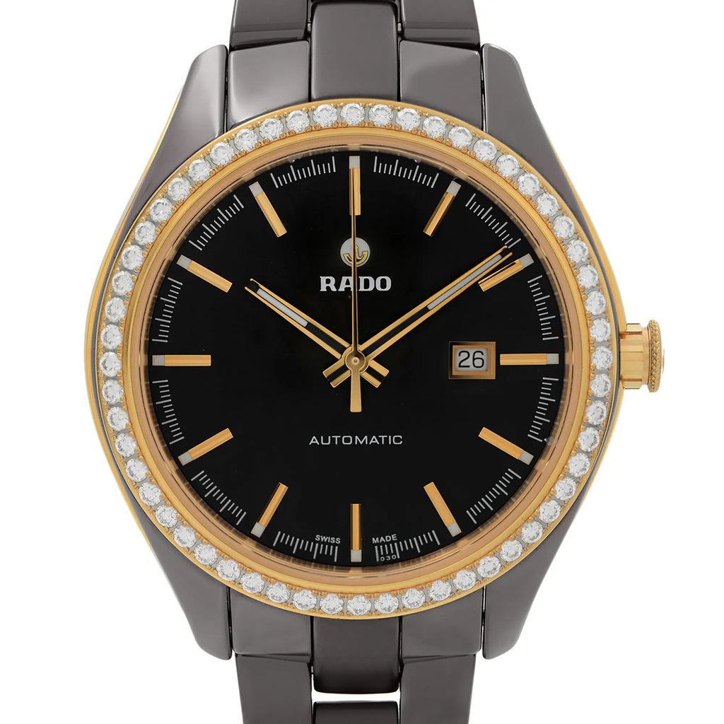 An image of a wristwatch taken from a front close-up angle, showcasing the watch face. The watch has a black dial with gold-tone hour markers and hands, featuring a date window at the 3 o'clock position. The bezel is adorned with small, sparkling stones, and the case is gold-toned with a metallic strap. The watch is in display model condition.