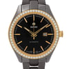 An image of a wristwatch taken from a front close-up angle, showcasing the watch face. The watch has a black dial with gold-tone hour markers and hands, featuring a date window at the 3 o'clock position. The bezel is adorned with small, sparkling stones, and the case is gold-toned with a metallic strap. The watch is in display model condition.
