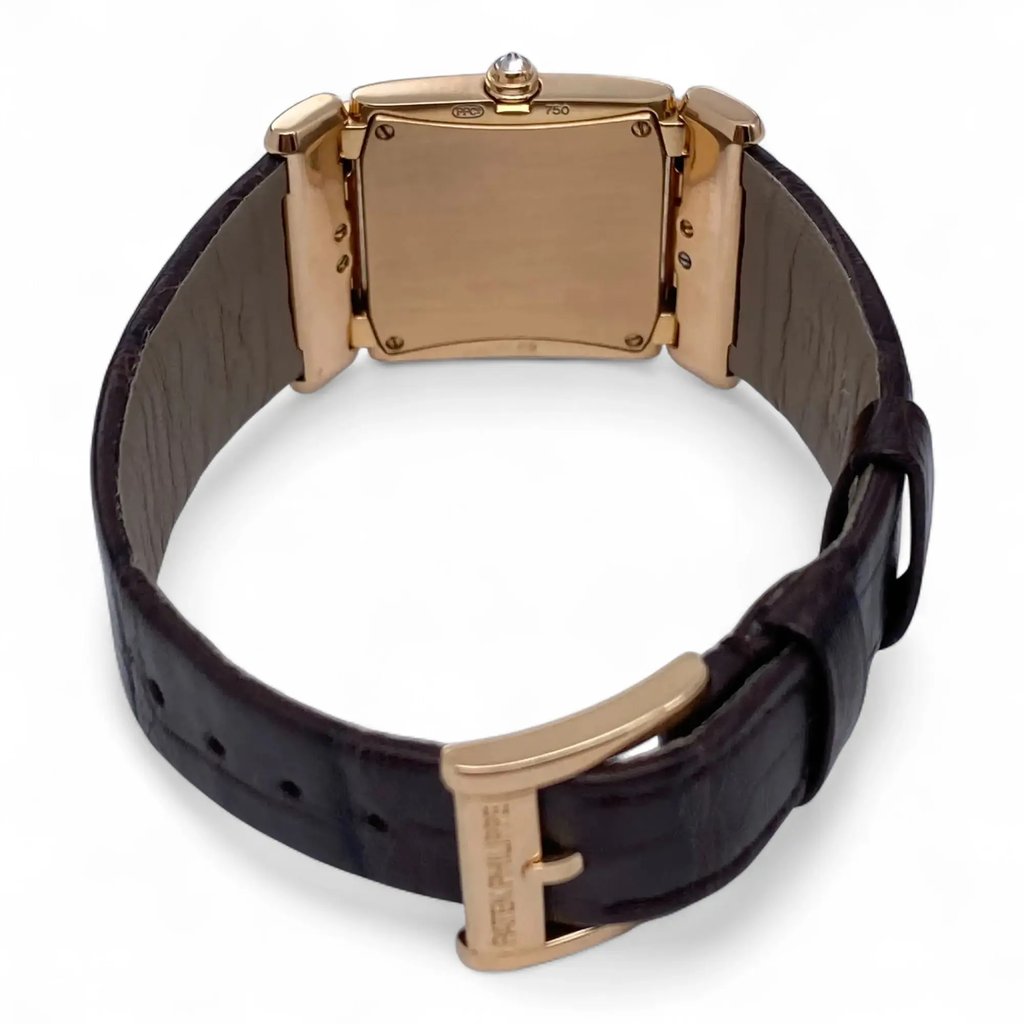 An image of a pre-owned Patek Philippe women's wristwatch viewed from the back, showcasing the closed case and brown leather strap. The watch is positioned upright, with the strap forming a circular shape. The angle is slightly elevated, providing a clear view of the gold buckle and the back of the case, highlighting its smooth texture and polished finish. The distance is close, focusing on the details of the watch's craftsmanship.