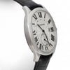 An image of a pre-owned Cartier men's wristwatch, captured from a slightly angled side view. The watch features a stainless steel case with a black leather strap. The dial displays large Roman numerals and a date indicator. The photograph is taken from a close distance, showcasing the watch's elegant design and details.