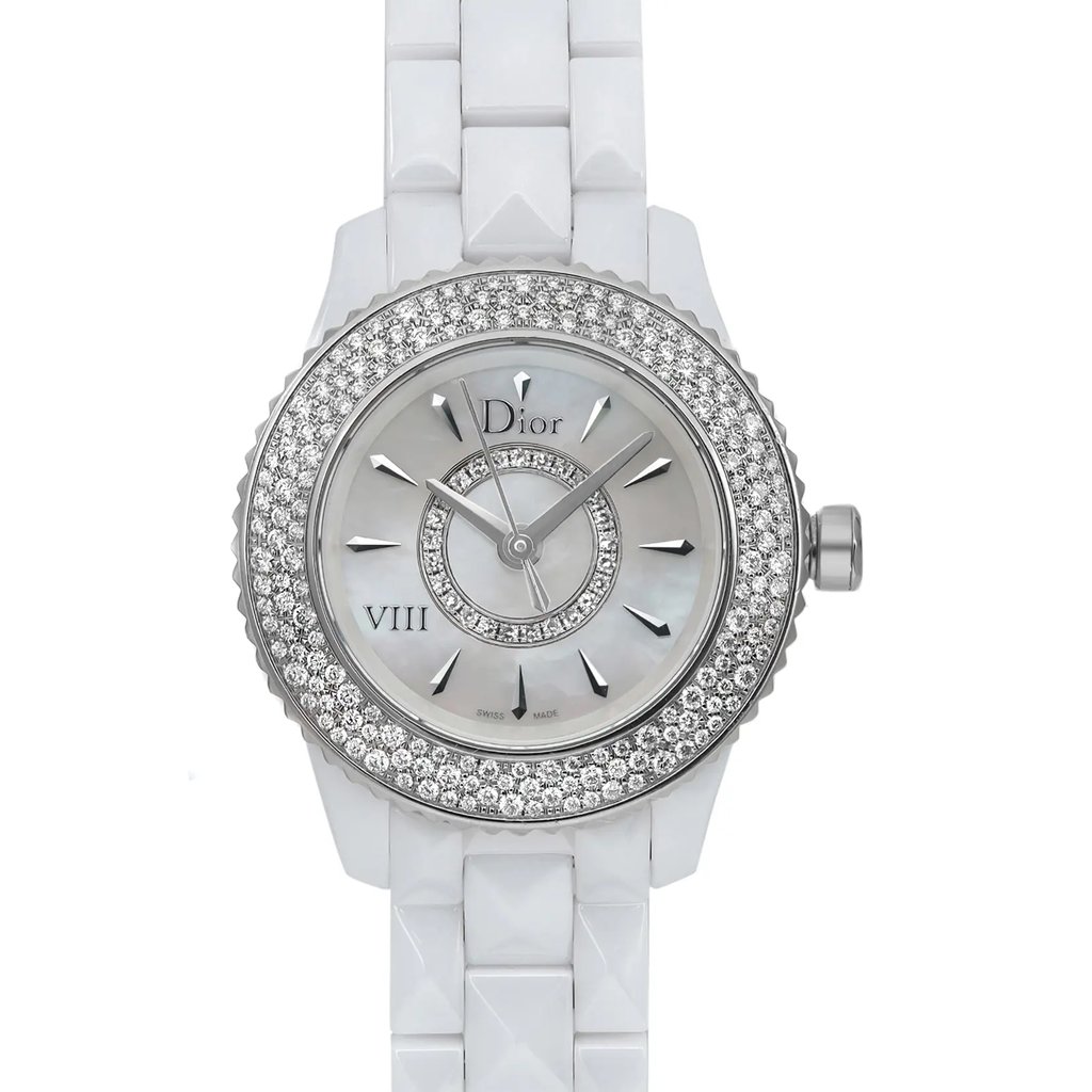 An image of a pre-owned wristwatch viewed from the front at a close-up angle, showcasing the watch face. The watch features a white band and a dial surrounded by two concentric circles of small, sparkling stones. The brand name is visible on the dial.