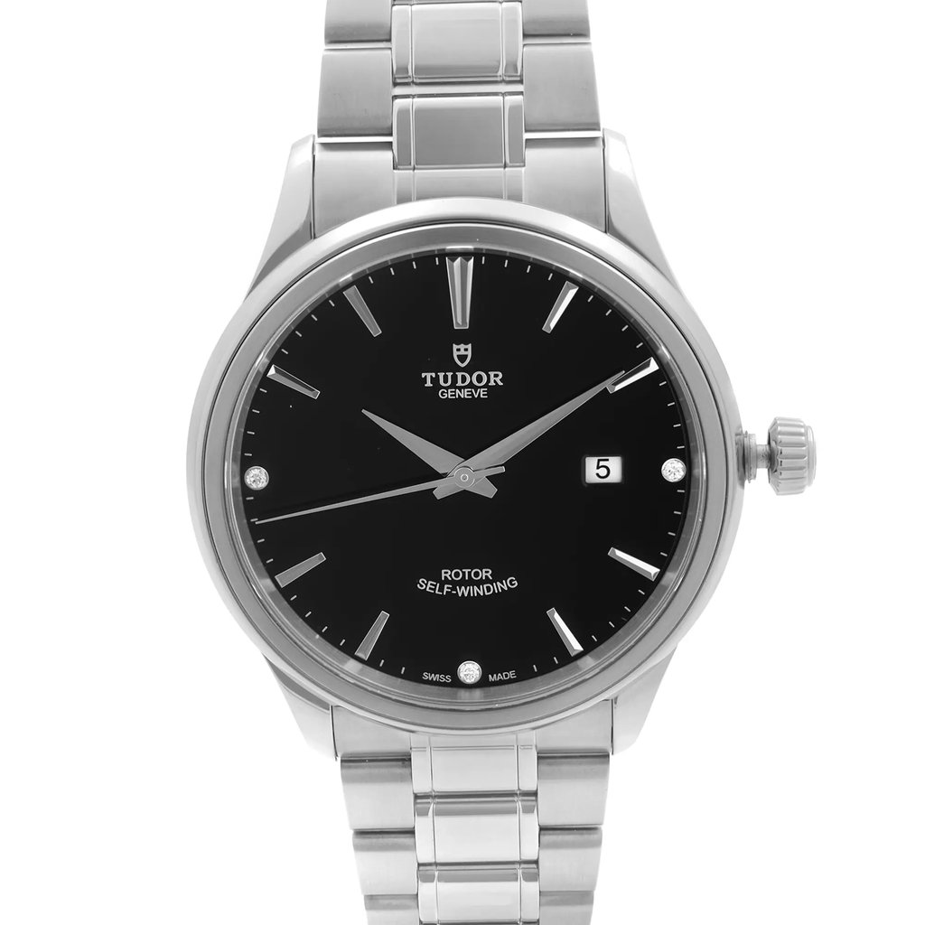 An image of a pre-owned men's TUDOR wristwatch displayed from a front angle, showcasing its sleek design. The watch has a black dial with silver hour markers and hands, and features a date indicator at the 3 o'clock position. It is equipped with a stainless steel bracelet and casing, positioned centrally in the frame for a clear and detailed view.